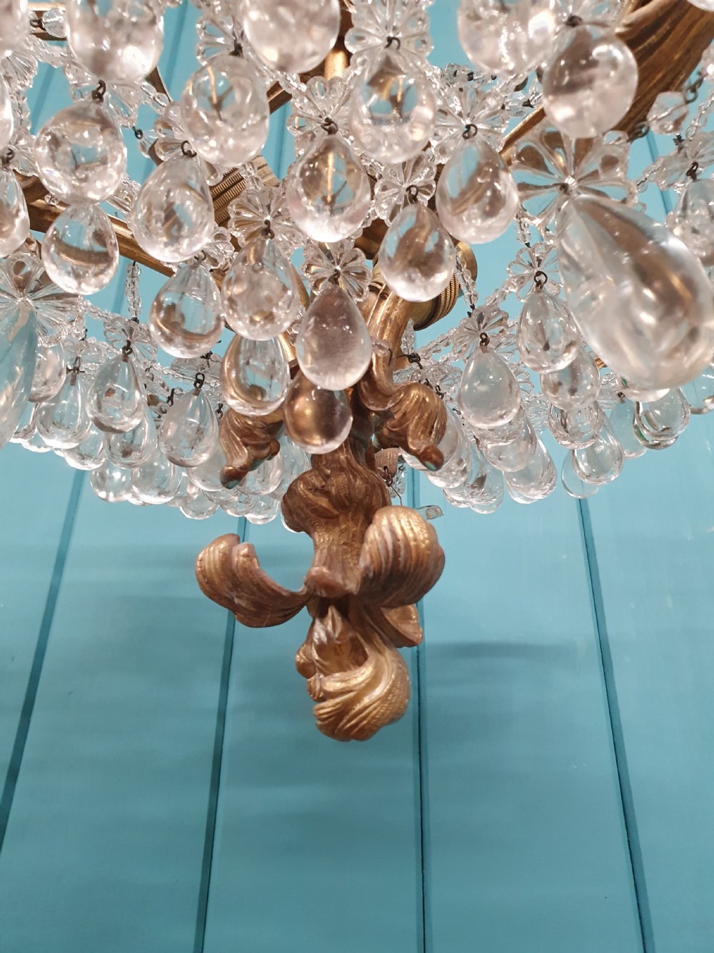 An early 20th-century gilded brass chandelier featuring sweeping leaf-form arms and cascading clear glass teardrop and grape-form droplets. View VII