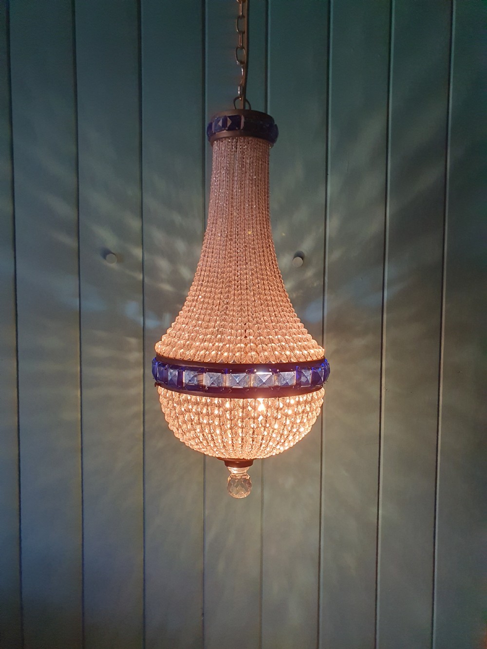 An early 20th-century beaded crystal basket chandelier featuring decorative bands of square-cut cobalt blue glass prisms and a brass frame. View V