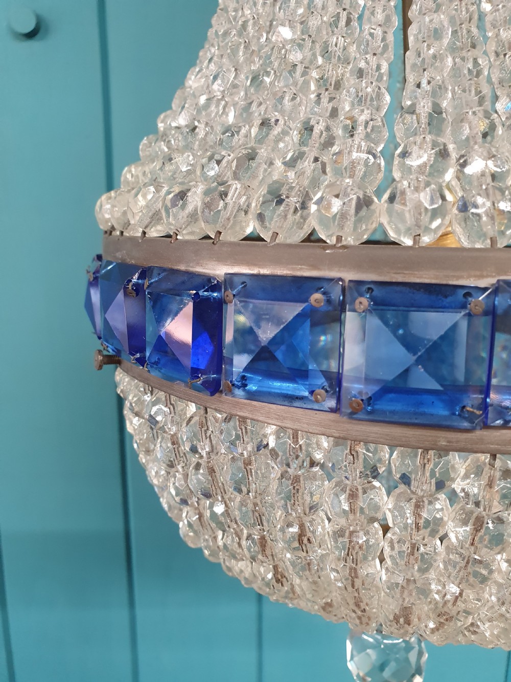An early 20th-century beaded crystal basket chandelier featuring decorative bands of square-cut cobalt blue glass prisms and a brass frame. View VI