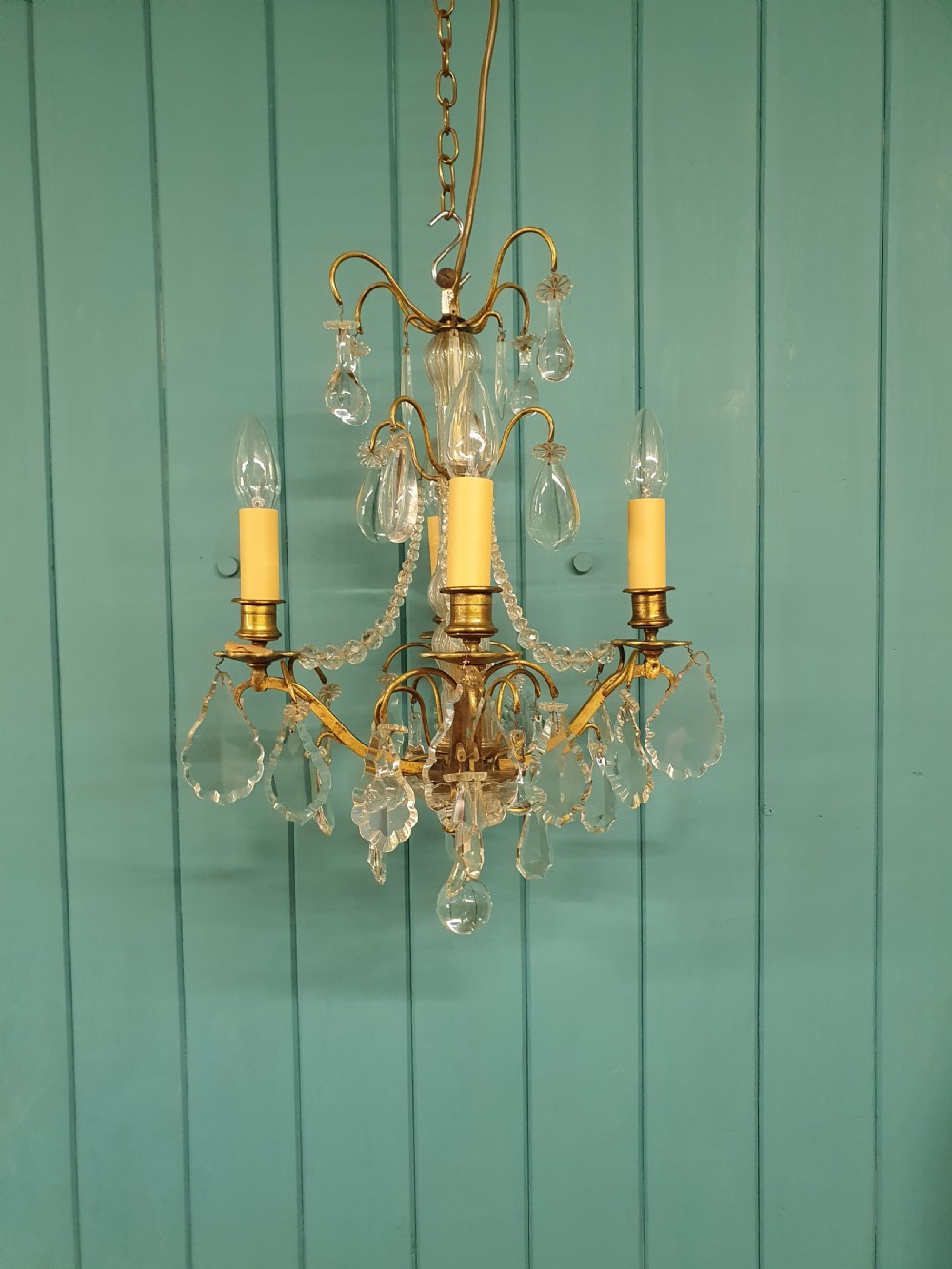 An antique French brass and crystal chandelier featuring curved scroll arms, a central glass stem, candle sleeves, and hanging teardrop glass prisms.
