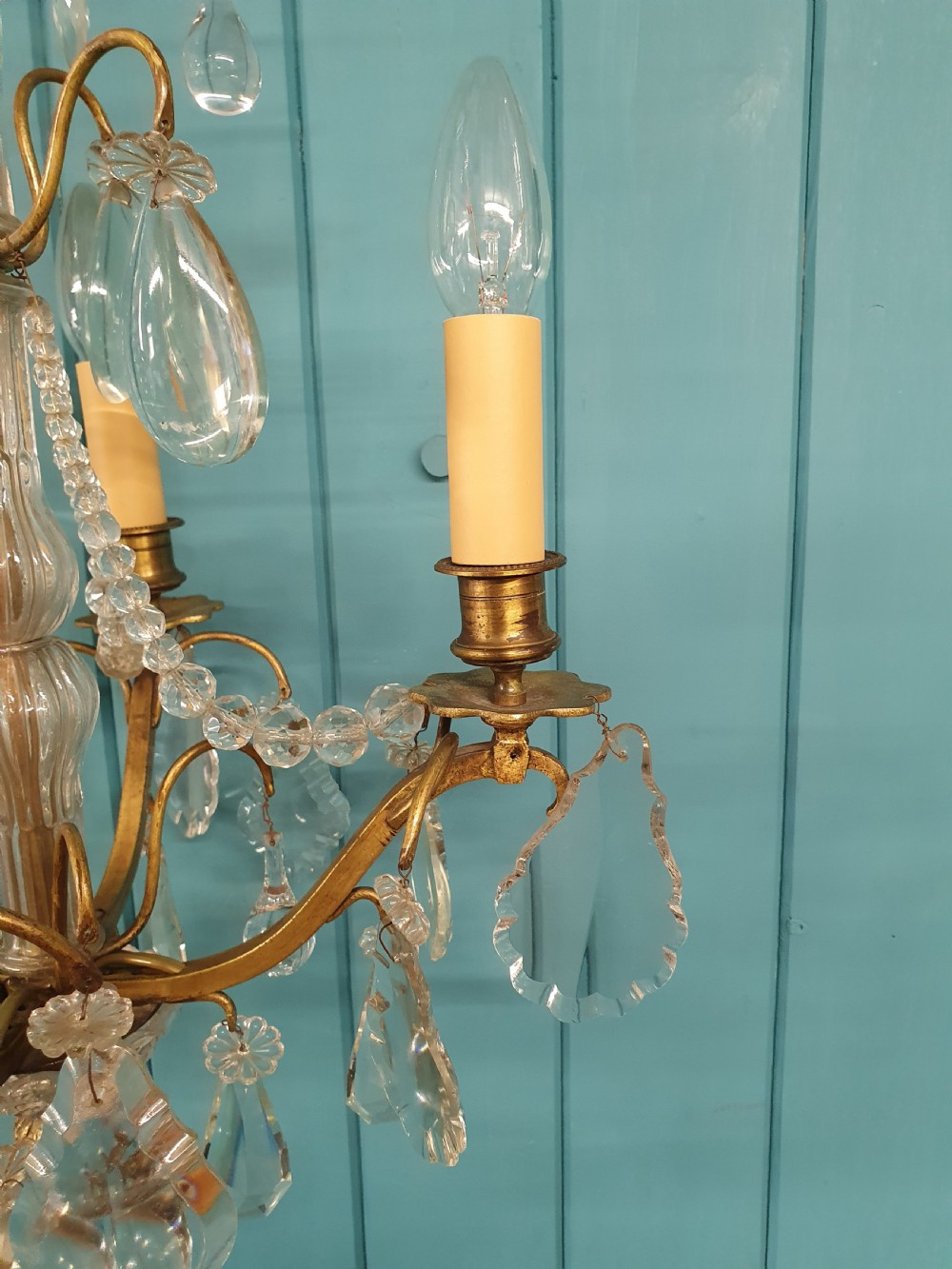 An antique French brass and crystal chandelier featuring curved scroll arms, a central glass stem, candle sleeves, and hanging teardrop glass prisms. View II