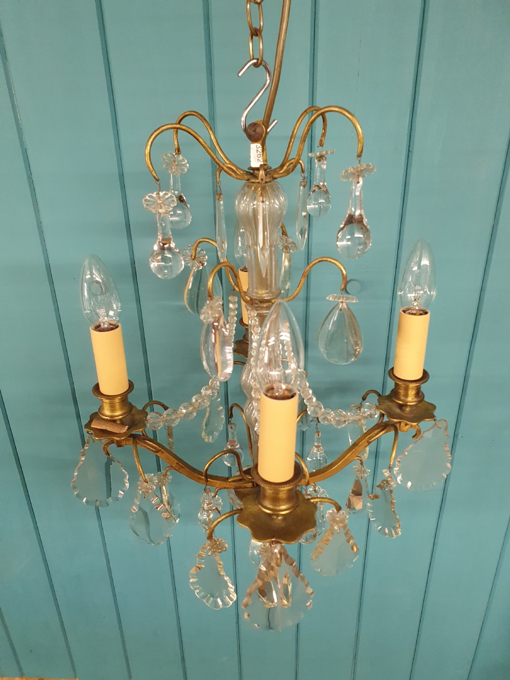 An antique French brass and crystal chandelier featuring curved scroll arms, a central glass stem, candle sleeves, and hanging teardrop glass prisms. View III