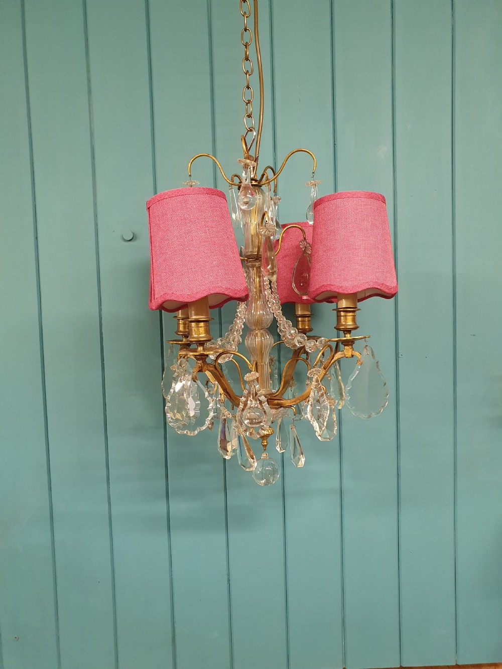 An antique French brass and crystal chandelier featuring curved scroll arms, a central glass stem, candle sleeves, and hanging teardrop glass prisms. View VII