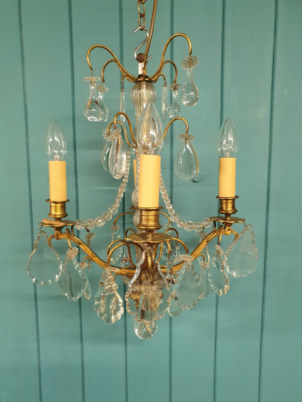 An antique French brass and crystal chandelier featuring curved scroll arms, a central glass stem, candle sleeves, and hanging teardrop glass prisms. View VIII