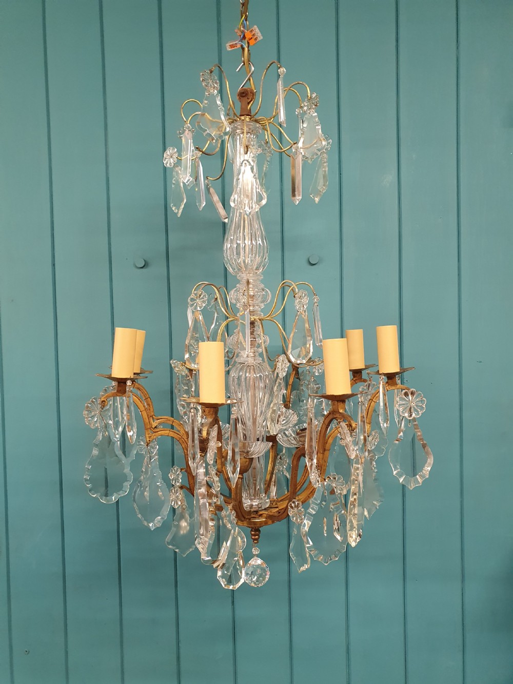 An early twentieth-century French eight-arm glass crystal chandelier featuring a central baluster stem, scrolling metal arms, and suspended cut glass drops.