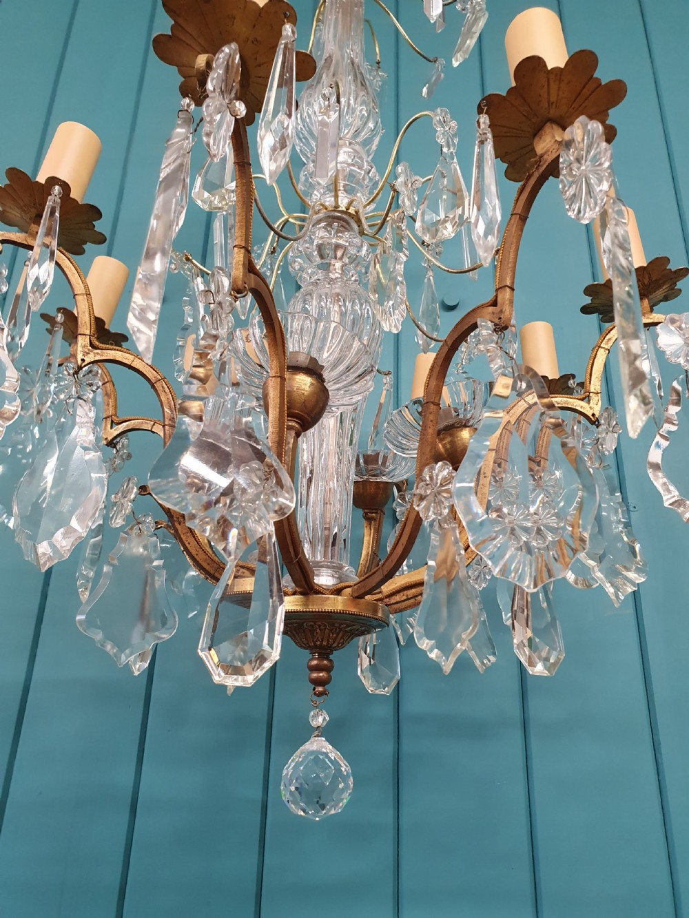 An early twentieth-century French eight-arm glass crystal chandelier featuring a central baluster stem, scrolling metal arms, and suspended cut glass drops. View V