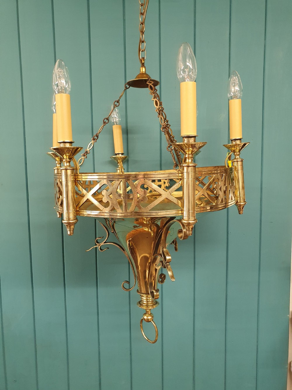 An early twentieth-century Gothic style brass chandelier featuring a pierced geometric gallery, central conical base, and five candle-style bulb holders suspended by chains.