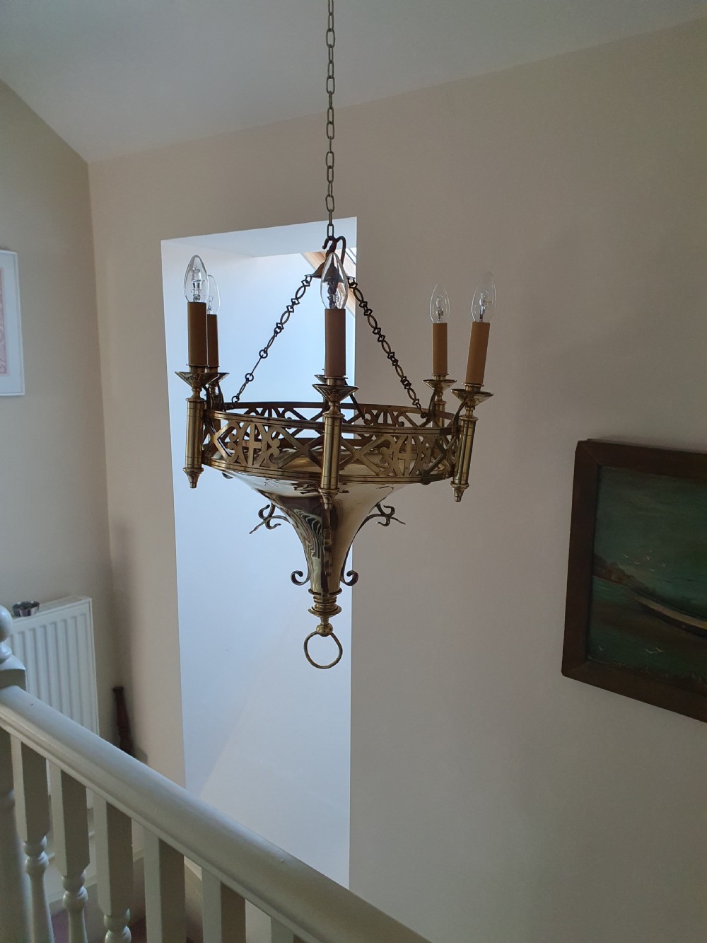 An early twentieth-century Gothic style brass chandelier featuring a pierced geometric gallery, central conical base, and five candle-style bulb holders suspended by chains. View V