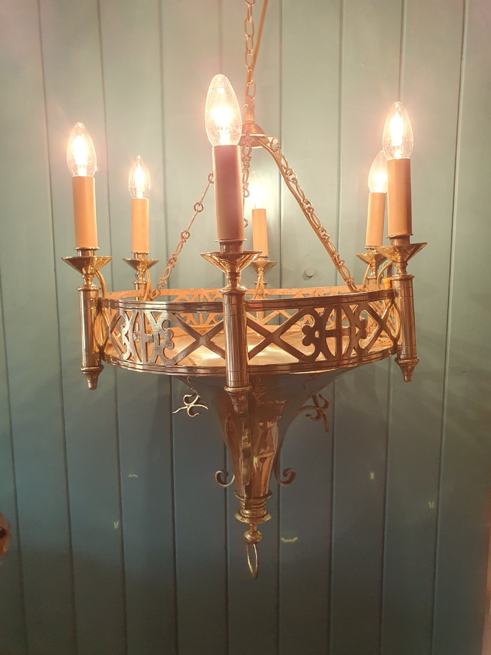 An early twentieth-century Gothic style brass chandelier featuring a pierced geometric gallery, central conical base, and five candle-style bulb holders suspended by chains. View VII