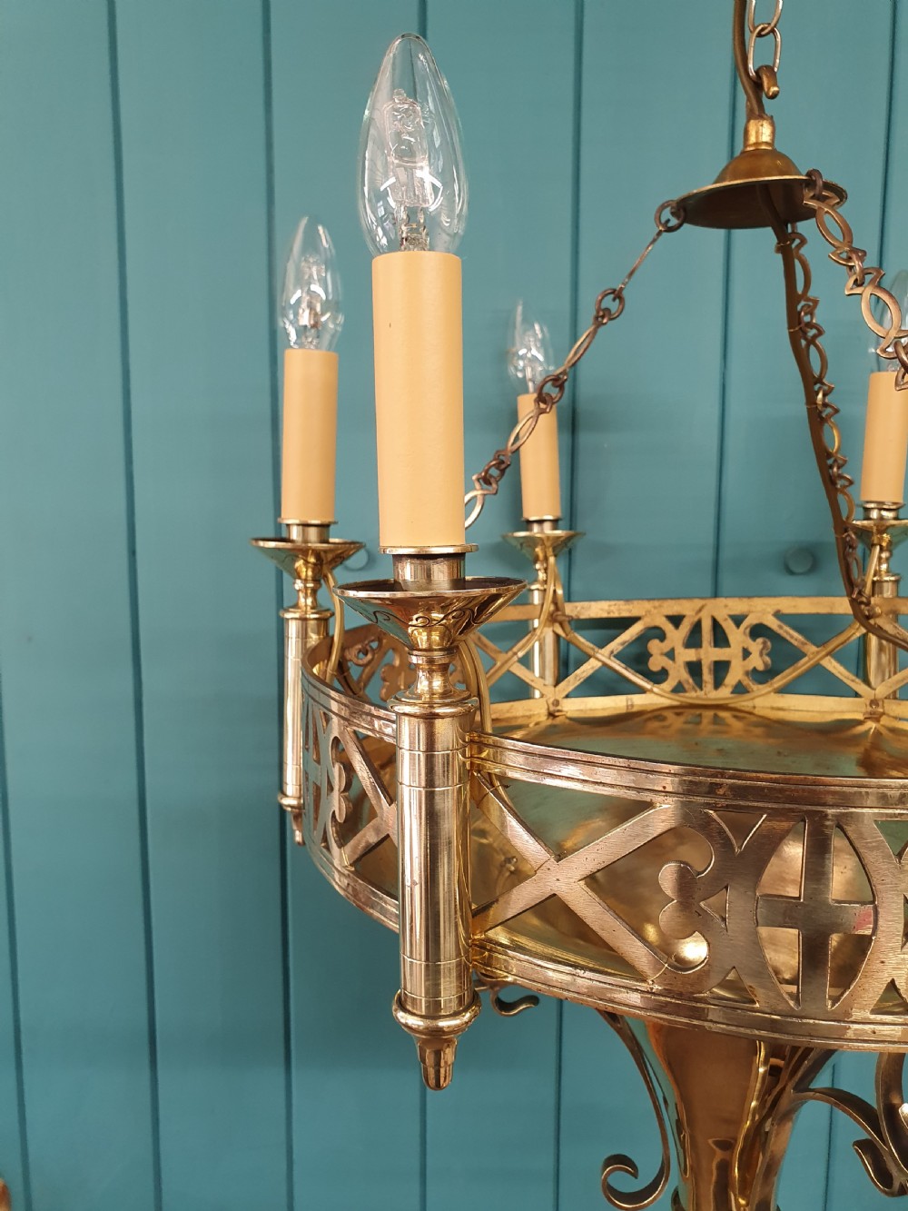 An early twentieth-century Gothic style brass chandelier featuring a pierced geometric gallery, central conical base, and five candle-style bulb holders suspended by chains. View VIII