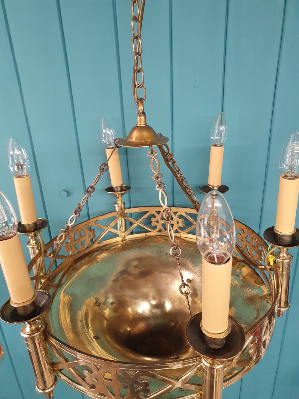 An early twentieth-century Gothic style brass chandelier featuring a pierced geometric gallery, central conical base, and five candle-style bulb holders suspended by chains. View X