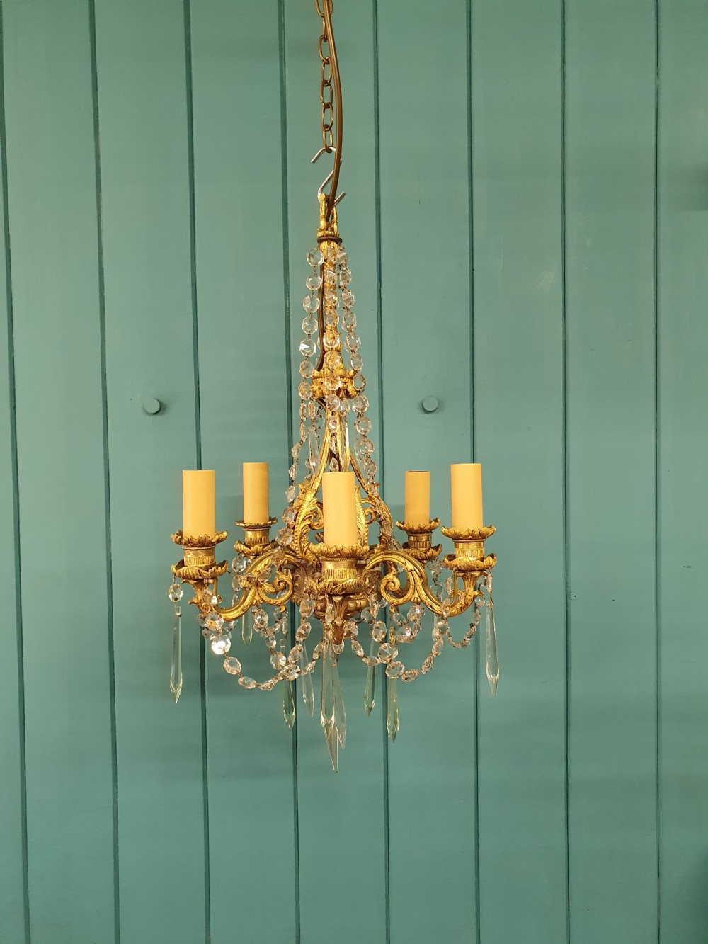 An early 20th-century small gilt brass five-arm chandelier decorated with clear glass crystal swags and teardrop pendants.