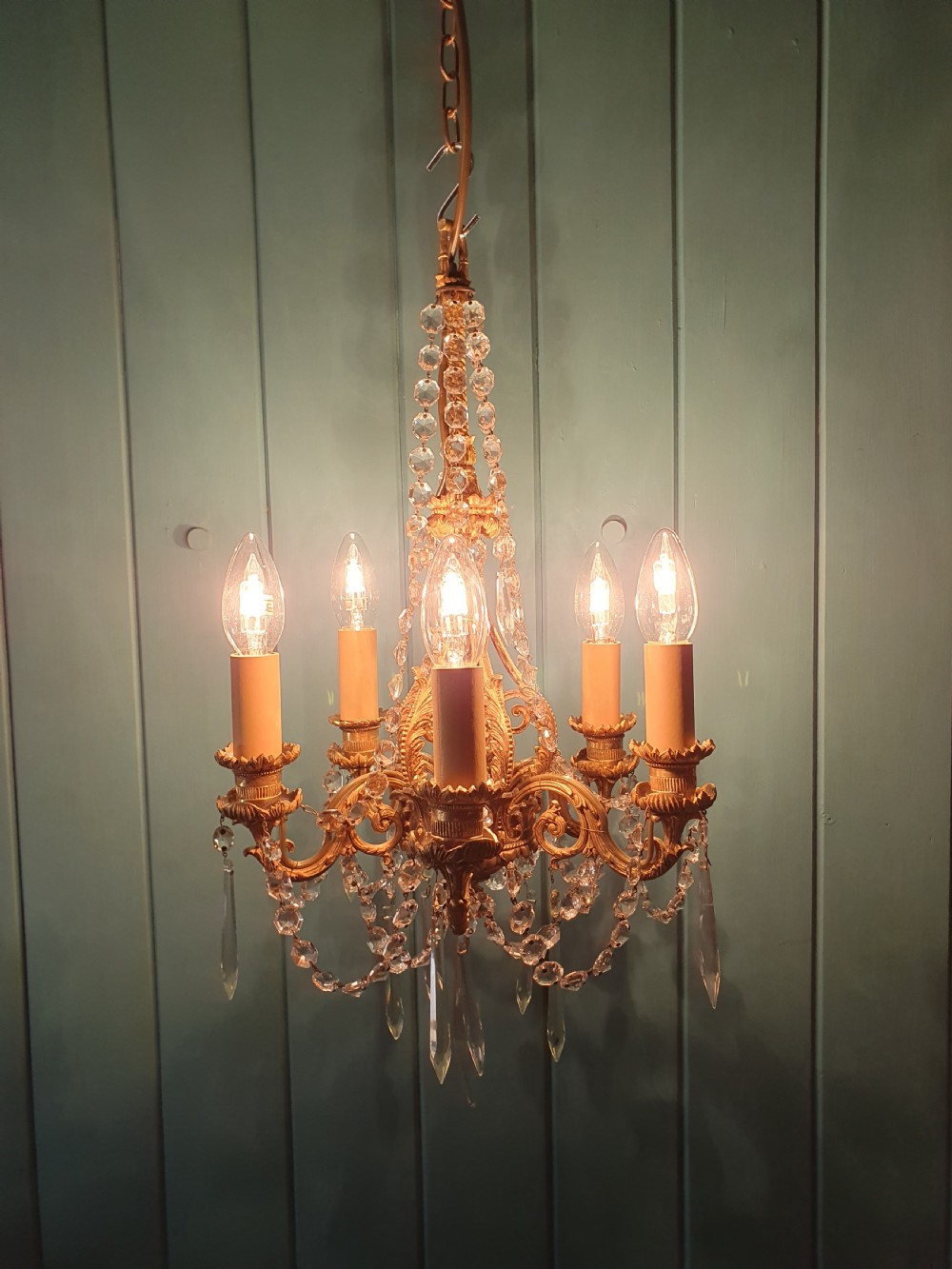An early 20th-century small gilt brass five-arm chandelier decorated with clear glass crystal swags and teardrop pendants. View IV