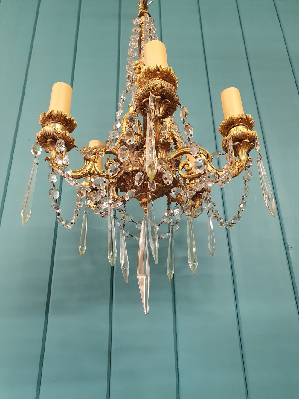 An early 20th-century small gilt brass five-arm chandelier decorated with clear glass crystal swags and teardrop pendants. View V