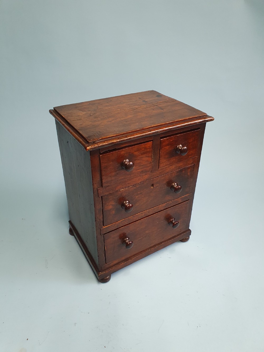 An early nineteenth-century miniature pine chest featuring two short drawers above two long drawers with turned wooden knobs and bun feet.