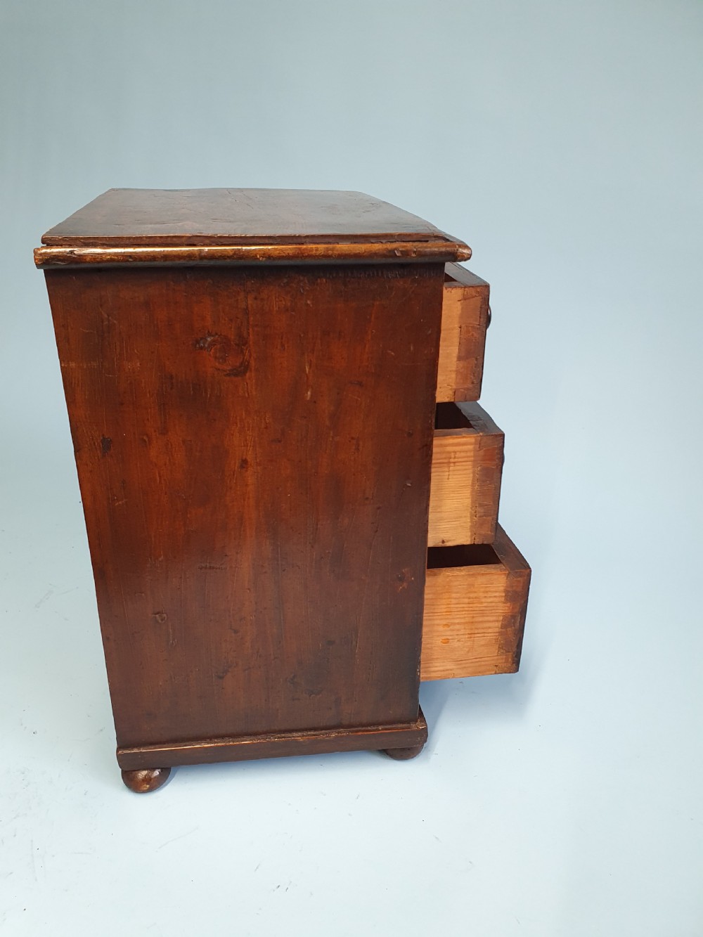 An early nineteenth-century miniature pine chest featuring two short drawers above two long drawers with turned wooden knobs and bun feet. View II