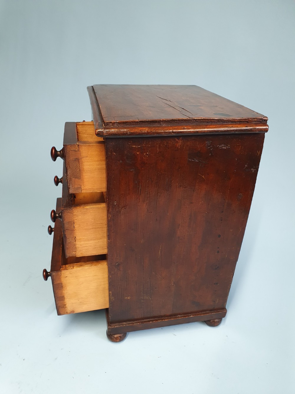 An early nineteenth-century miniature pine chest featuring two short drawers above two long drawers with turned wooden knobs and bun feet. View VIII