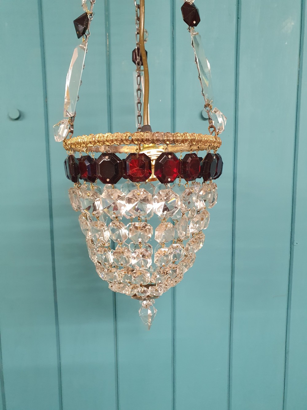 An early 20th-century cut glass basket chandelier suspended by chains, featuring a band of ruby red faceted glass accents above a tapered bead basket structure. View III