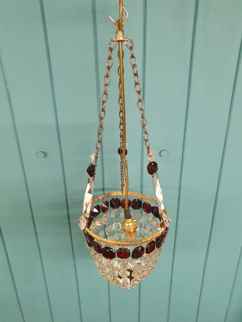 An early 20th-century cut glass basket chandelier suspended by chains, featuring a band of ruby red faceted glass accents above a tapered bead basket structure. View VI