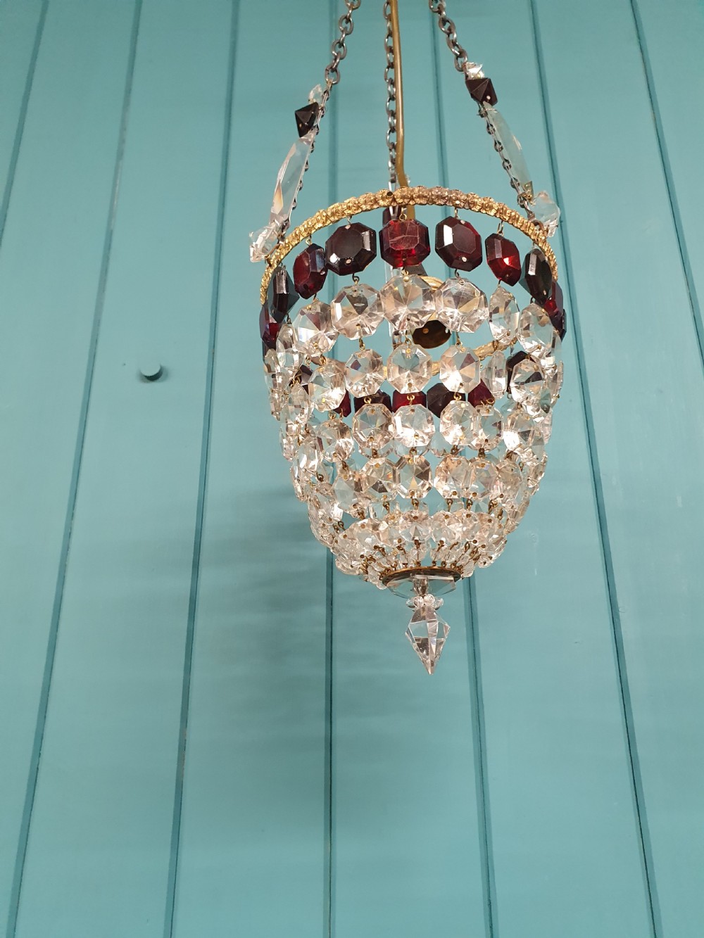 An early 20th-century cut glass basket chandelier suspended by chains, featuring a band of ruby red faceted glass accents above a tapered bead basket structure. View VII