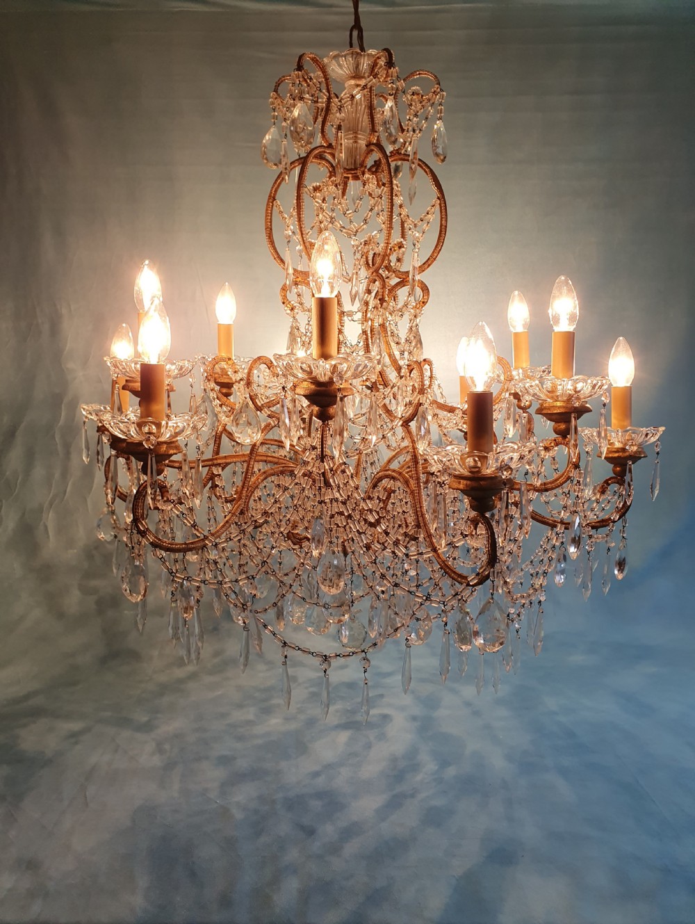 A twelve-arm gilt metal chandelier featuring cut glass crystal drops and beaded swags. View VI