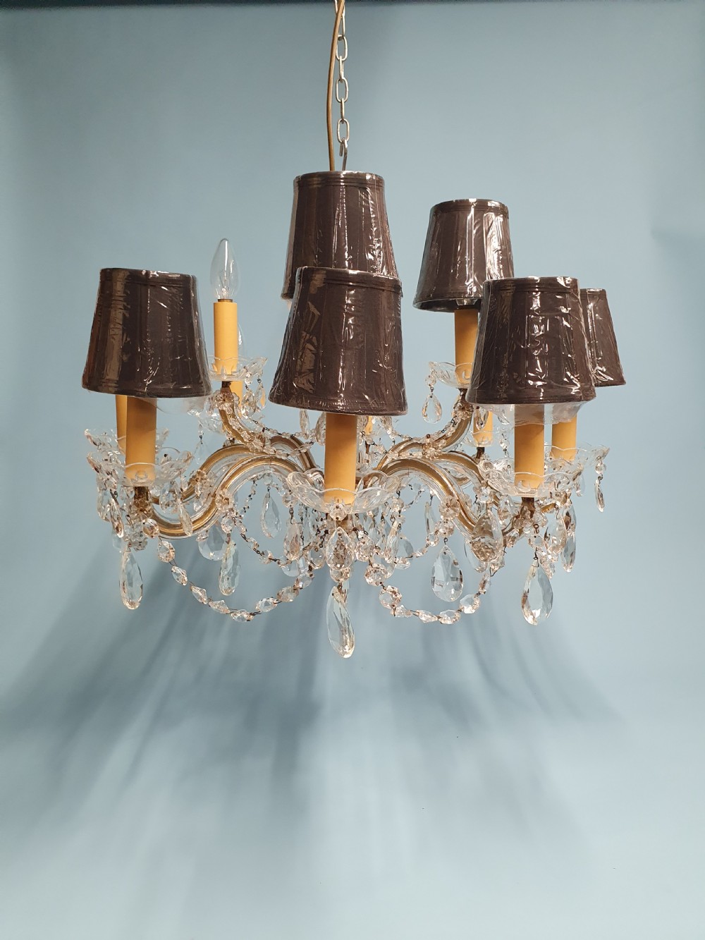 An early 20th-century two-tier crystal chandelier featuring twelve brass arms, glass drops, faux candle sleeves, and dark fabric shades.