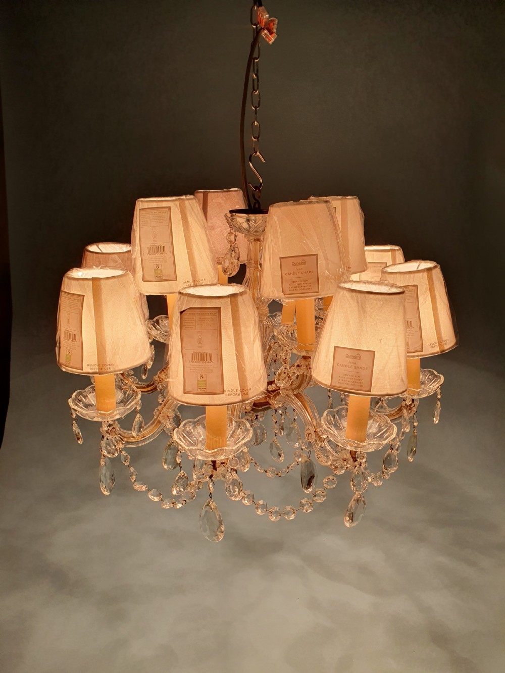 An early 20th-century two-tier crystal chandelier featuring twelve brass arms, glass drops, faux candle sleeves, and dark fabric shades. View IV