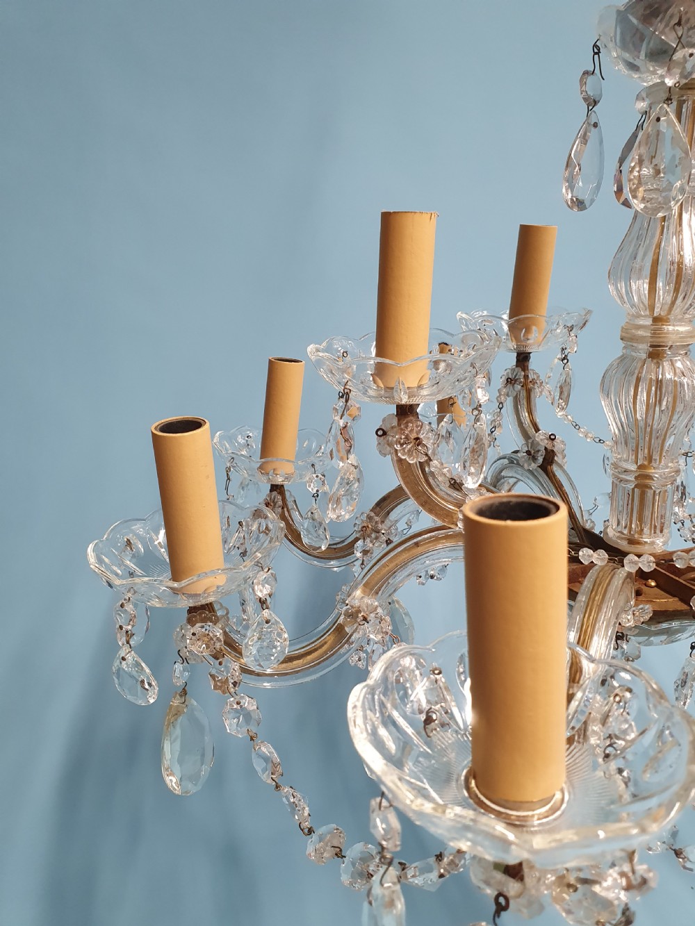 An early 20th-century two-tier crystal chandelier featuring twelve brass arms, glass drops, faux candle sleeves, and dark fabric shades. View VI