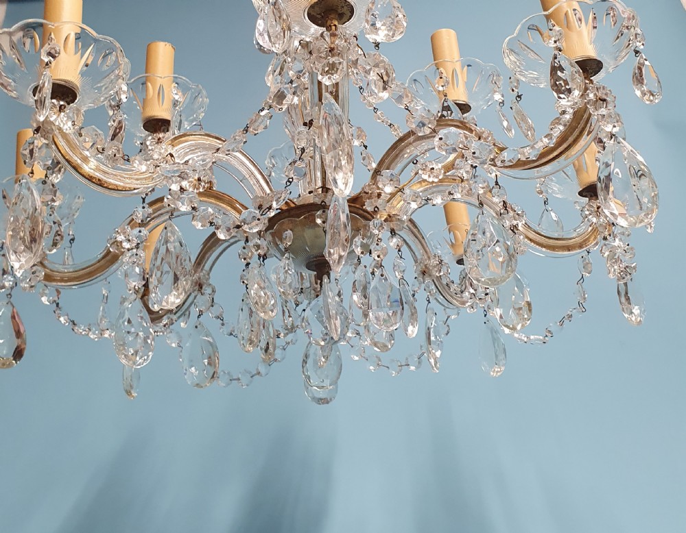 An early 20th-century two-tier crystal chandelier featuring twelve brass arms, glass drops, faux candle sleeves, and dark fabric shades. View VII