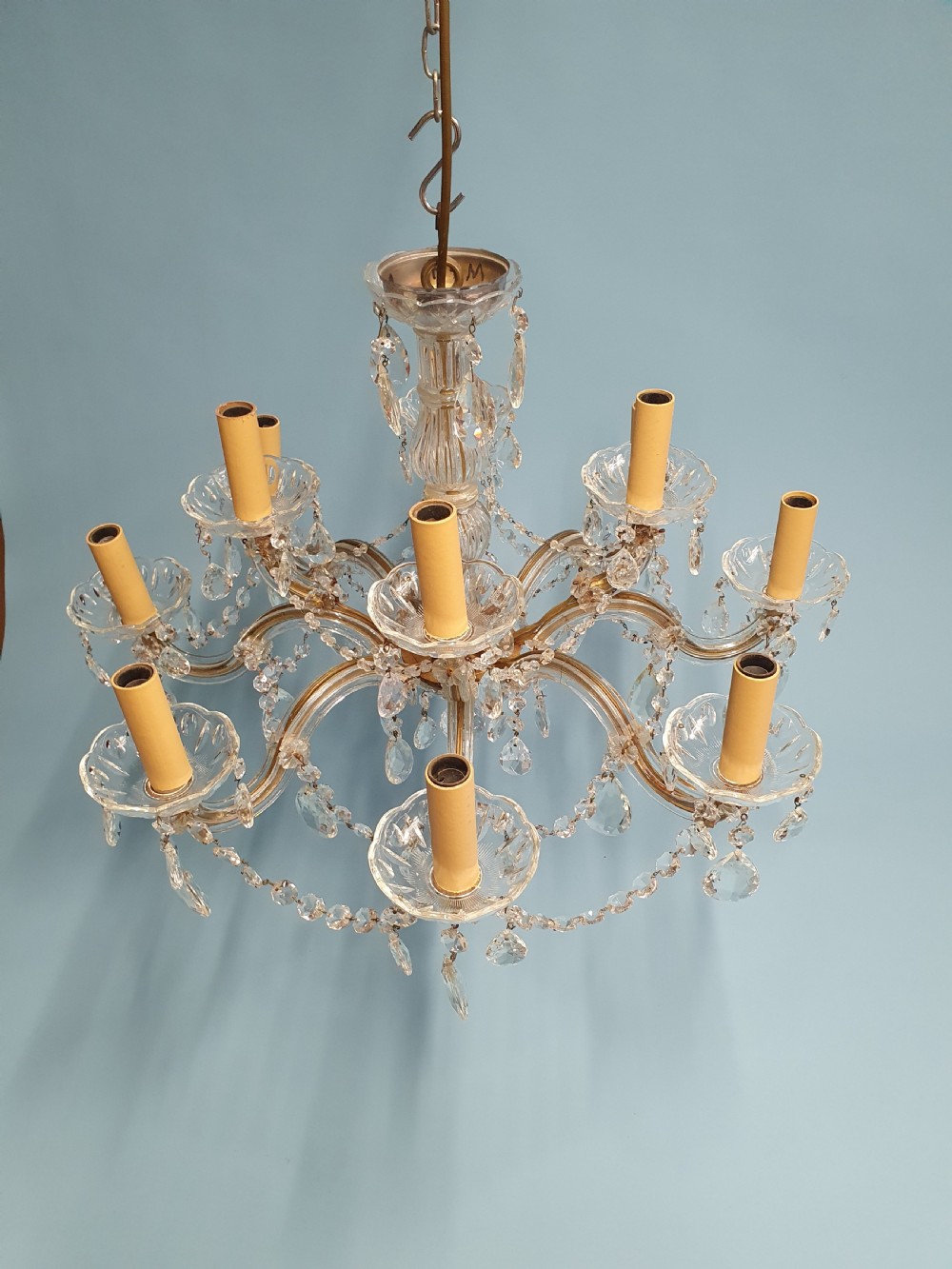 An early 20th-century two-tier crystal chandelier featuring twelve brass arms, glass drops, faux candle sleeves, and dark fabric shades. View VIII