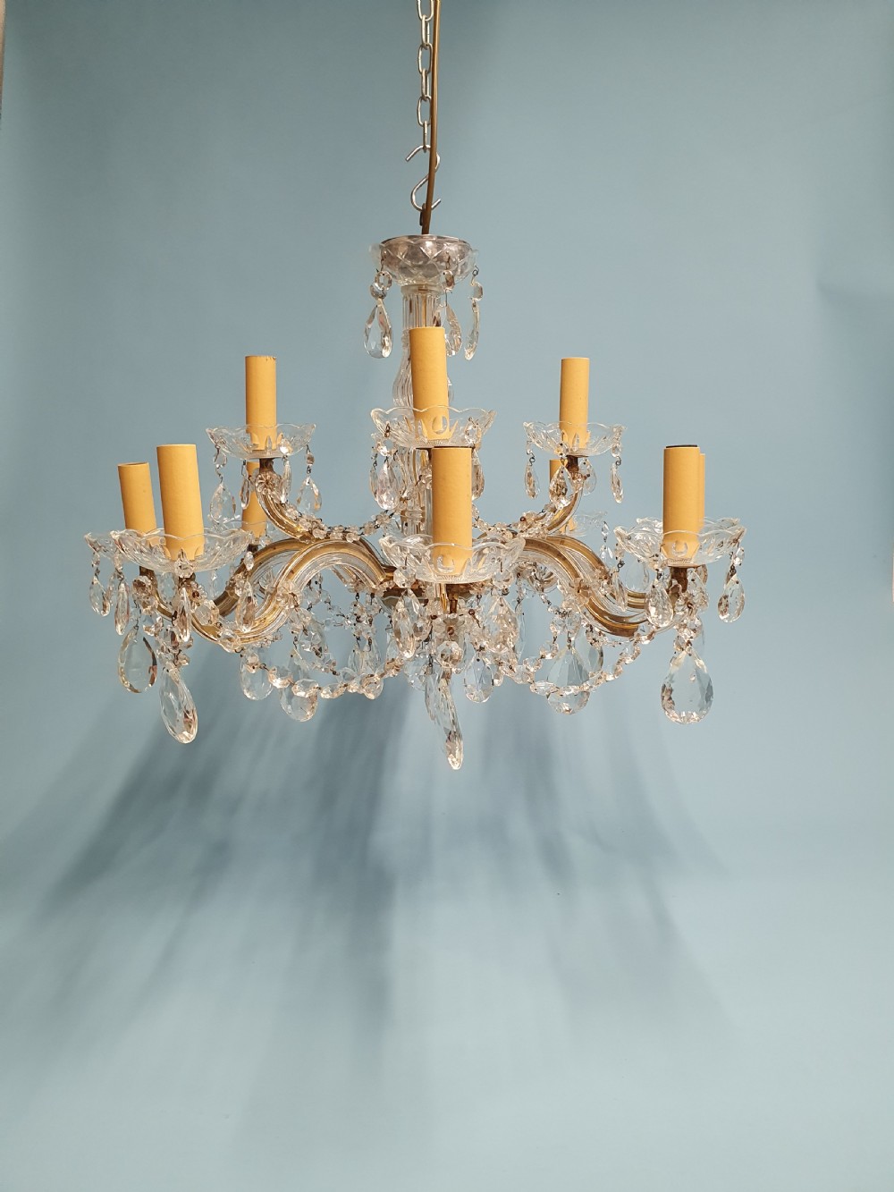 An early 20th-century two-tier crystal chandelier featuring twelve brass arms, glass drops, faux candle sleeves, and dark fabric shades. View IX