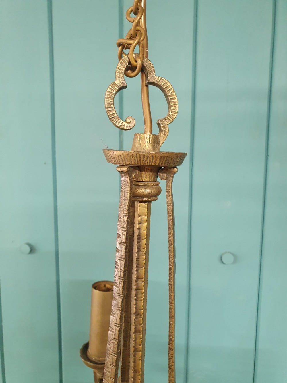 An Art Deco gilt brass three-arm chandelier featuring geometric central columns, candle-style bulb holders, and dangling teardrop accents. View VI
