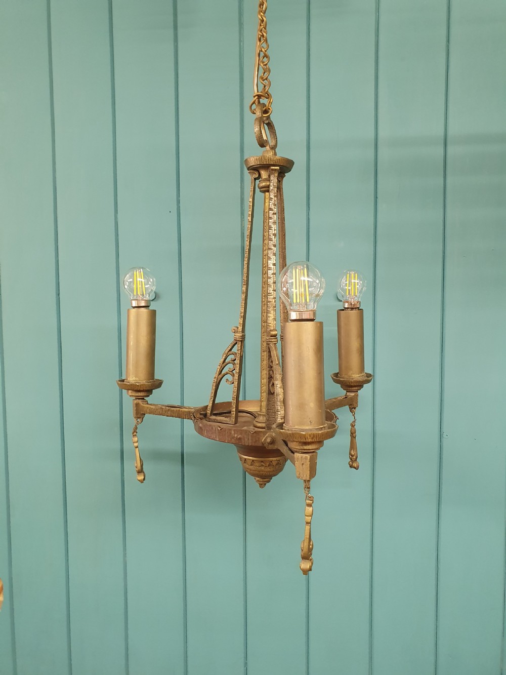 An Art Deco gilt brass three-arm chandelier featuring geometric central columns, candle-style bulb holders, and dangling teardrop accents. View VII