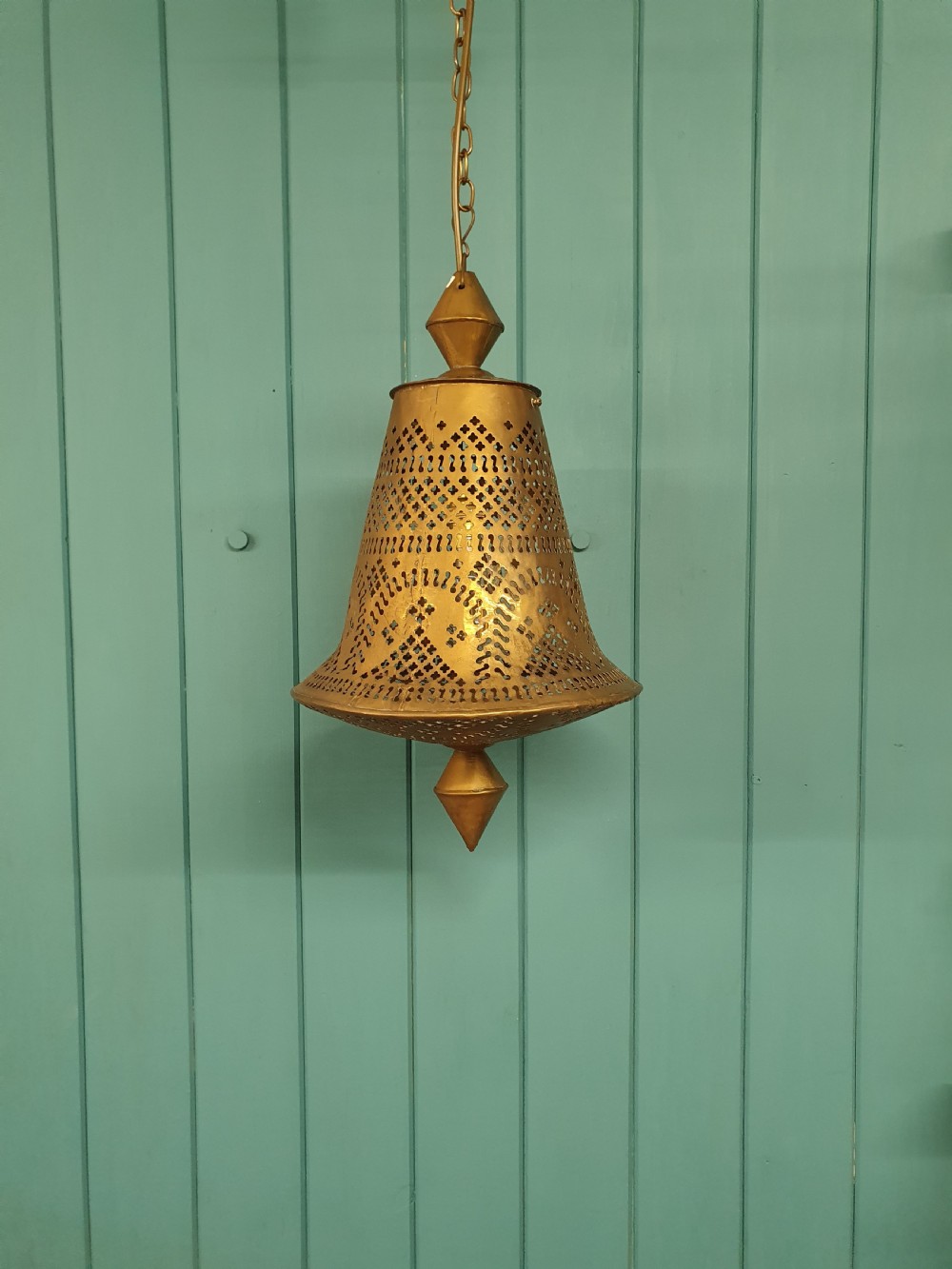 A flared bell-shaped pierced brass pendant light with geometric reticulated patterns suspended from a brass chain.