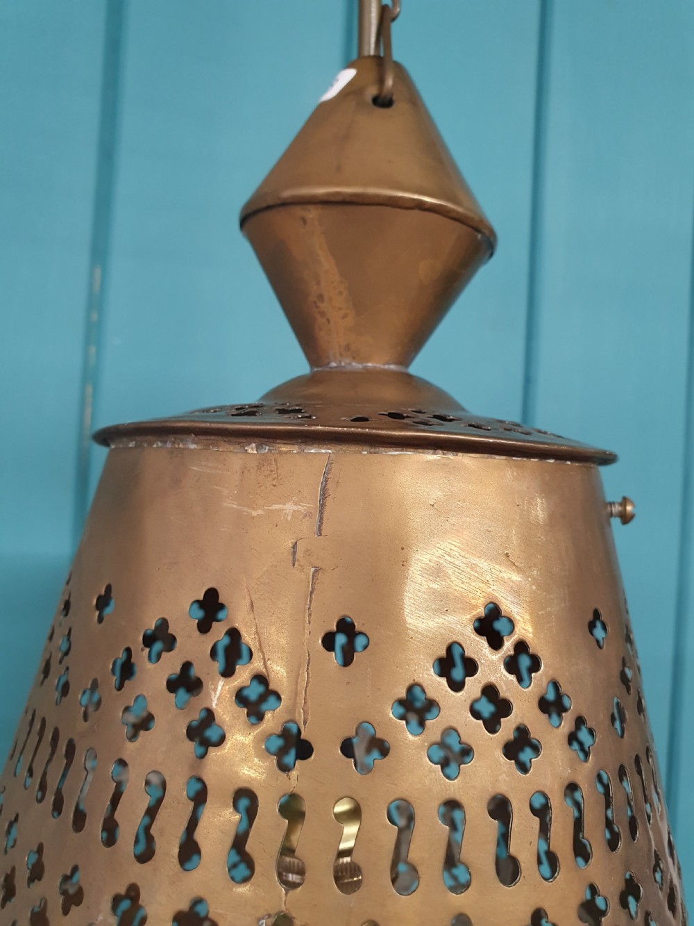 A flared bell-shaped pierced brass pendant light with geometric reticulated patterns suspended from a brass chain. View V