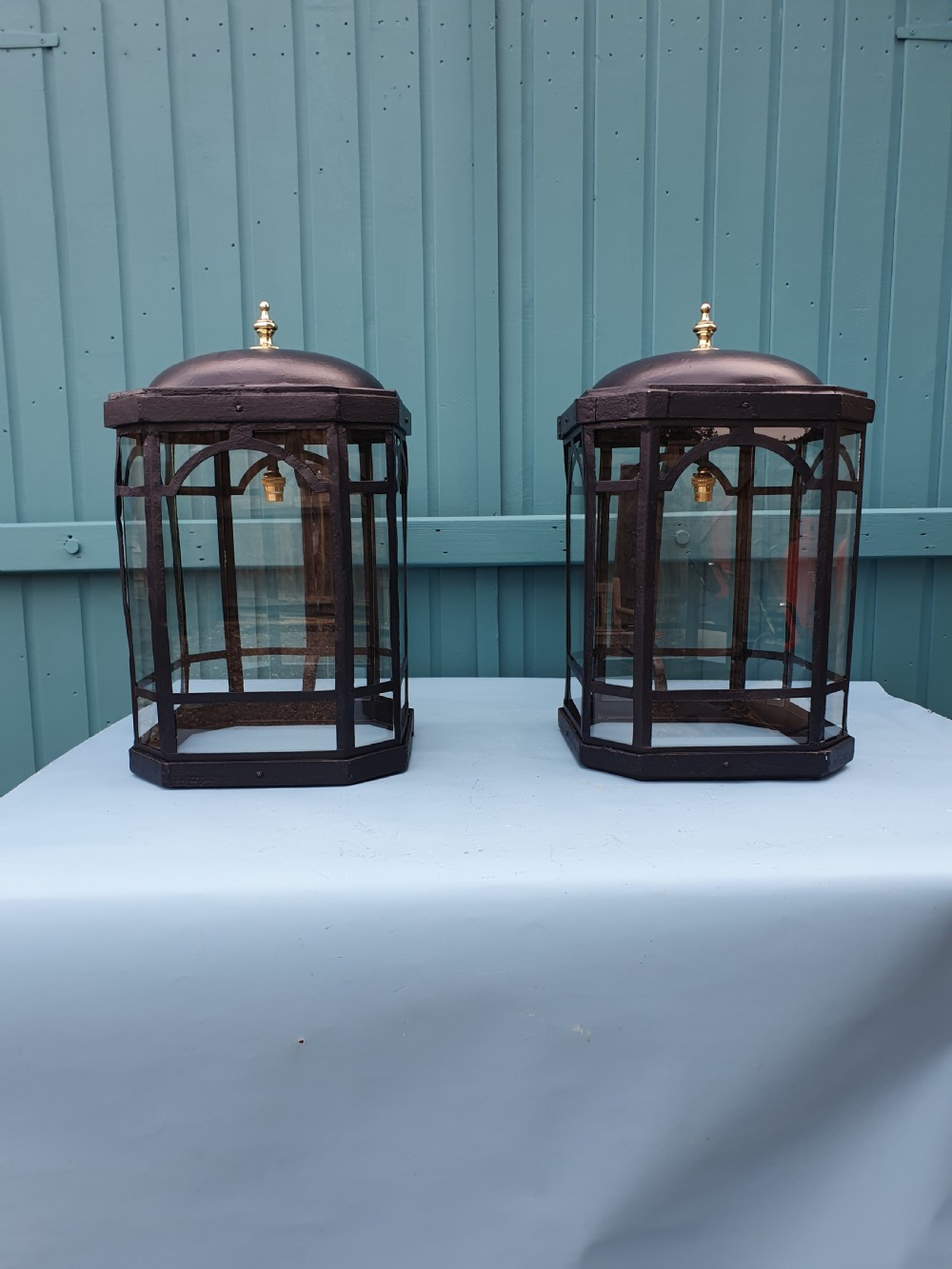 A pair of early 20th-century octagonal black wrought iron wall lanterns featuring clear glass panels, arched tracery, scrollwork brackets, and brass finials. View III