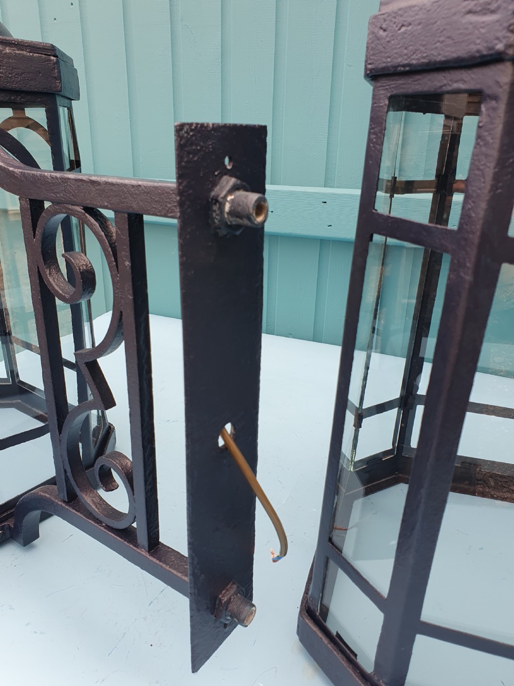A pair of early 20th-century octagonal black wrought iron wall lanterns featuring clear glass panels, arched tracery, scrollwork brackets, and brass finials. View VII