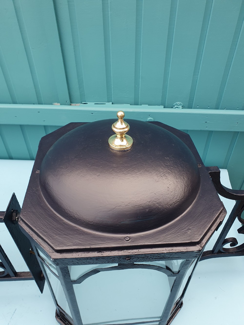 A pair of early 20th-century octagonal black wrought iron wall lanterns featuring clear glass panels, arched tracery, scrollwork brackets, and brass finials. View VIII