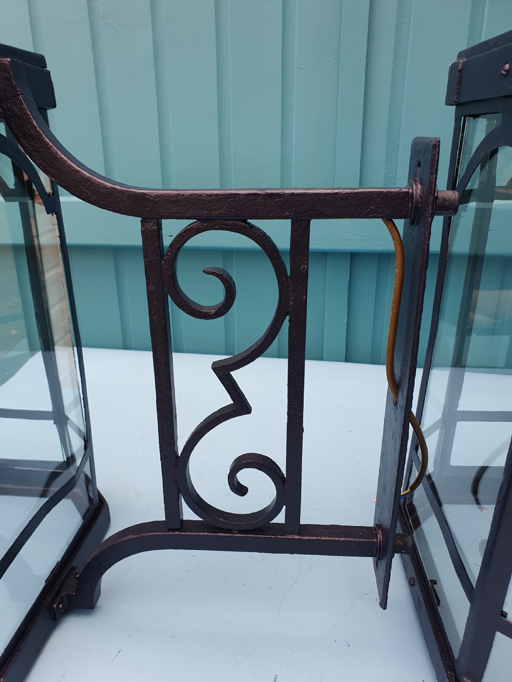 A pair of early 20th-century octagonal black wrought iron wall lanterns featuring clear glass panels, arched tracery, scrollwork brackets, and brass finials. View IX