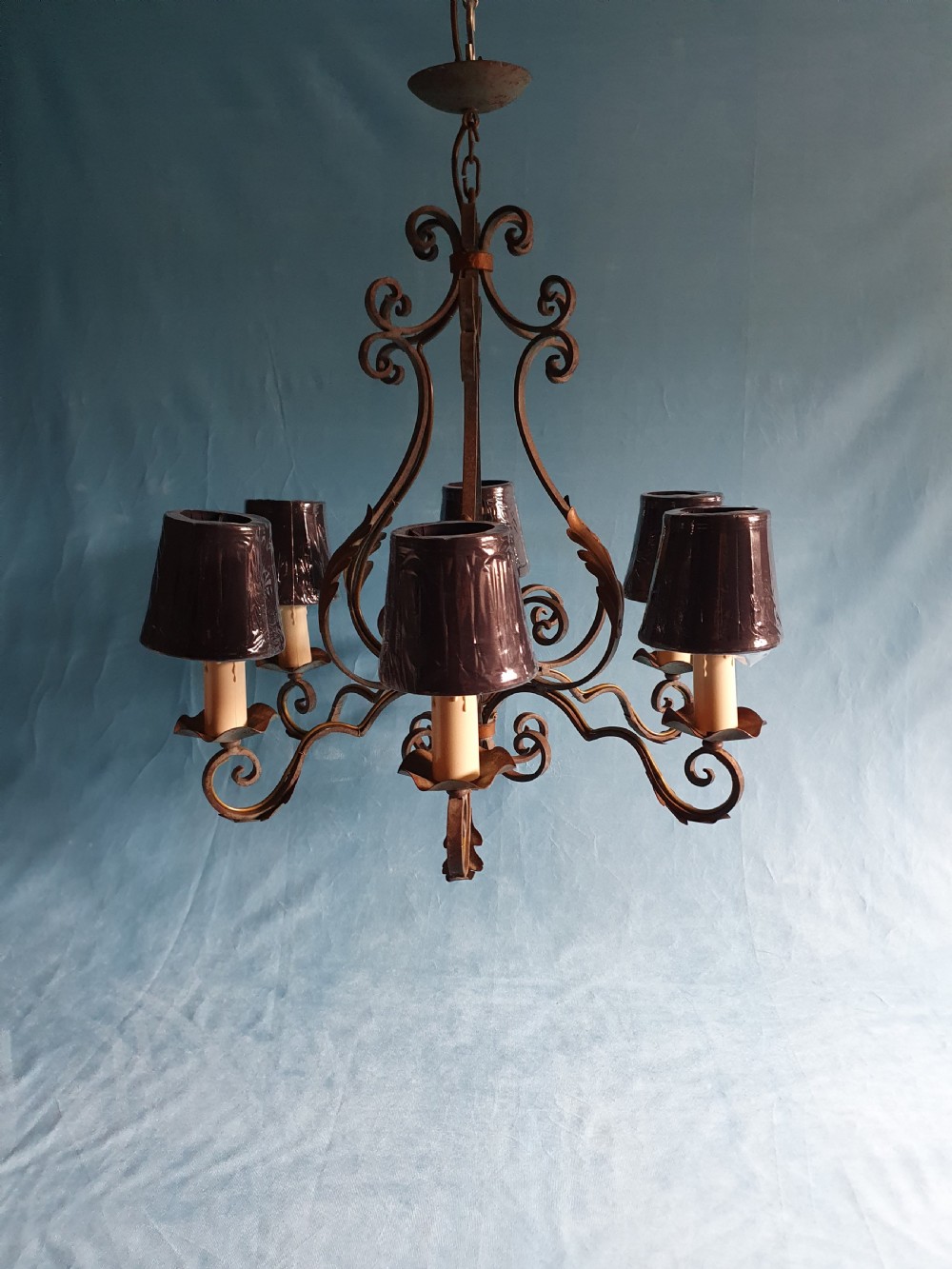 A dark green six-arm wrought steel chandelier with scrollwork arms, candle sleeves, and dark lampshades.