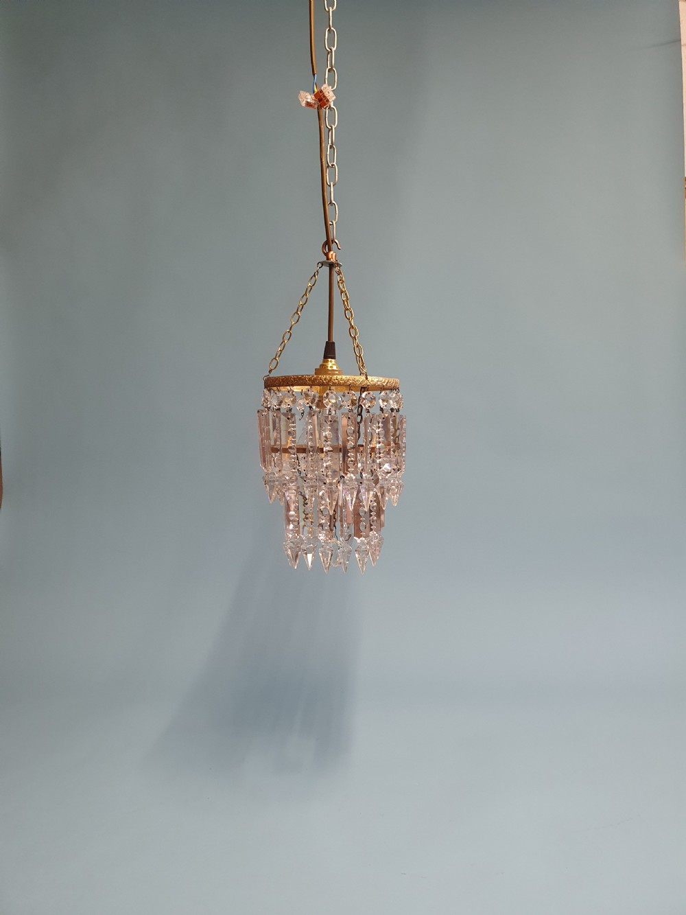 An early 20th-century brass ceiling pendant featuring tiered rows of faceted glass crystal droplets suspended by metal chains.
