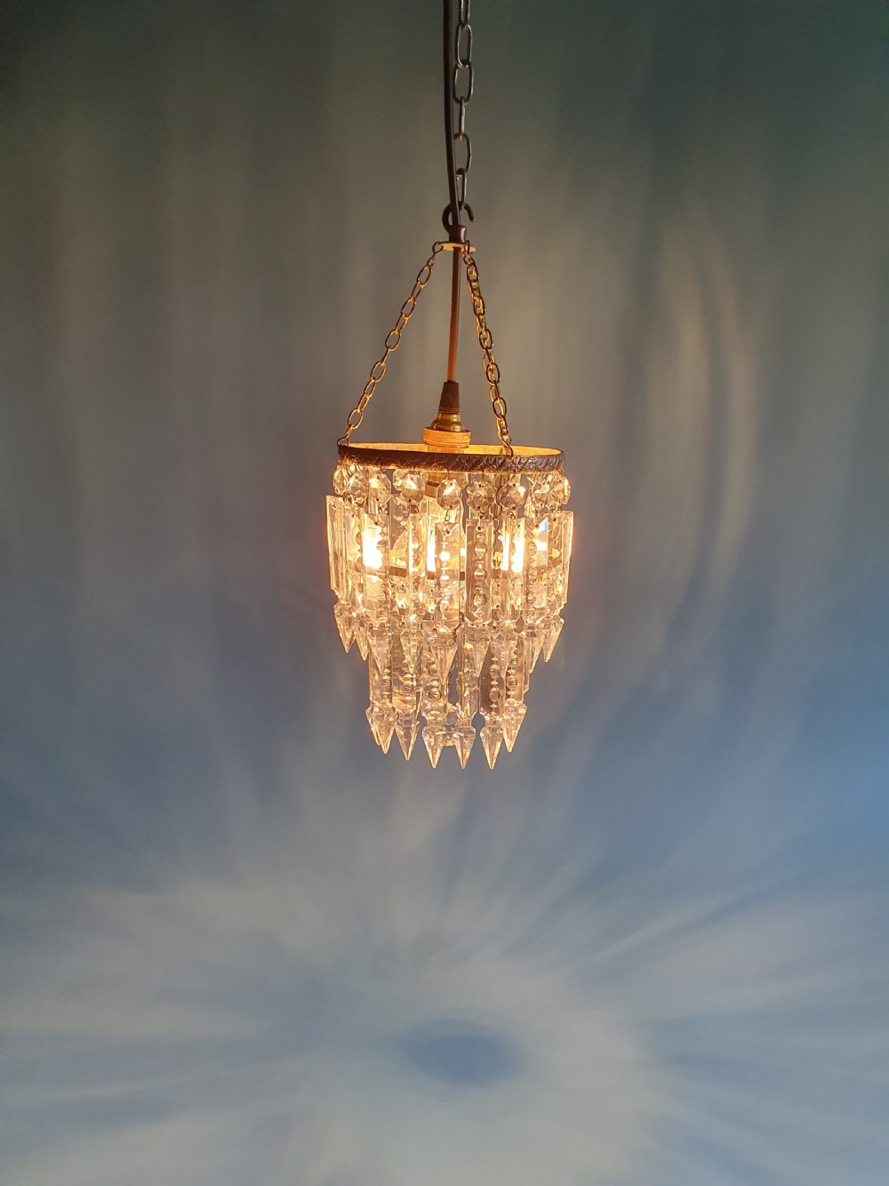 An early 20th-century brass ceiling pendant featuring tiered rows of faceted glass crystal droplets suspended by metal chains. View II