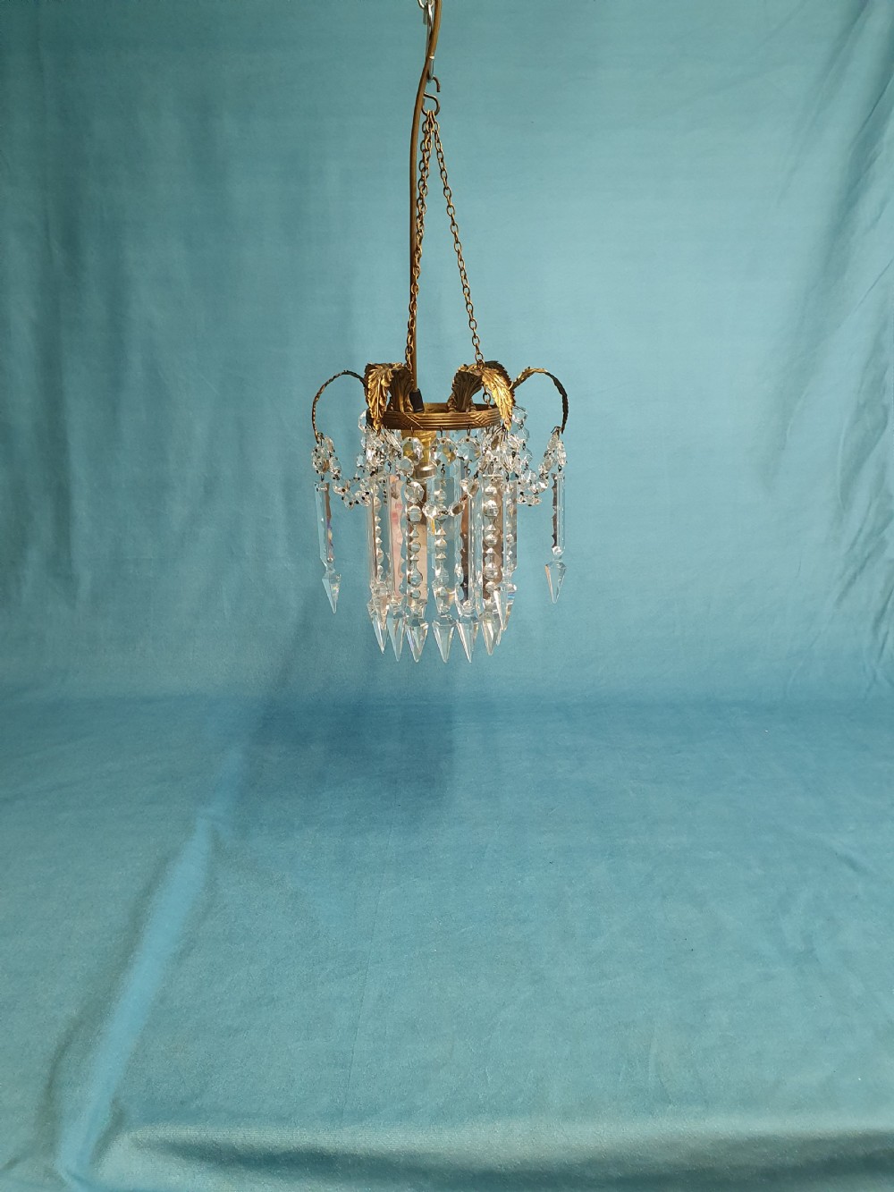 An early 20th-century small brass chandelier featuring acanthus leaf scroll arms suspending multiple tiers of clear faceted crystal prisms and droplets.