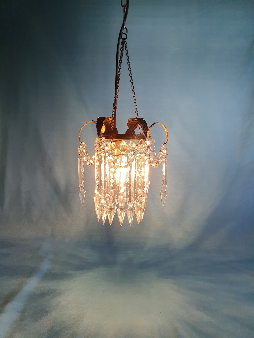 An early 20th-century small brass chandelier featuring acanthus leaf scroll arms suspending multiple tiers of clear faceted crystal prisms and droplets. View II