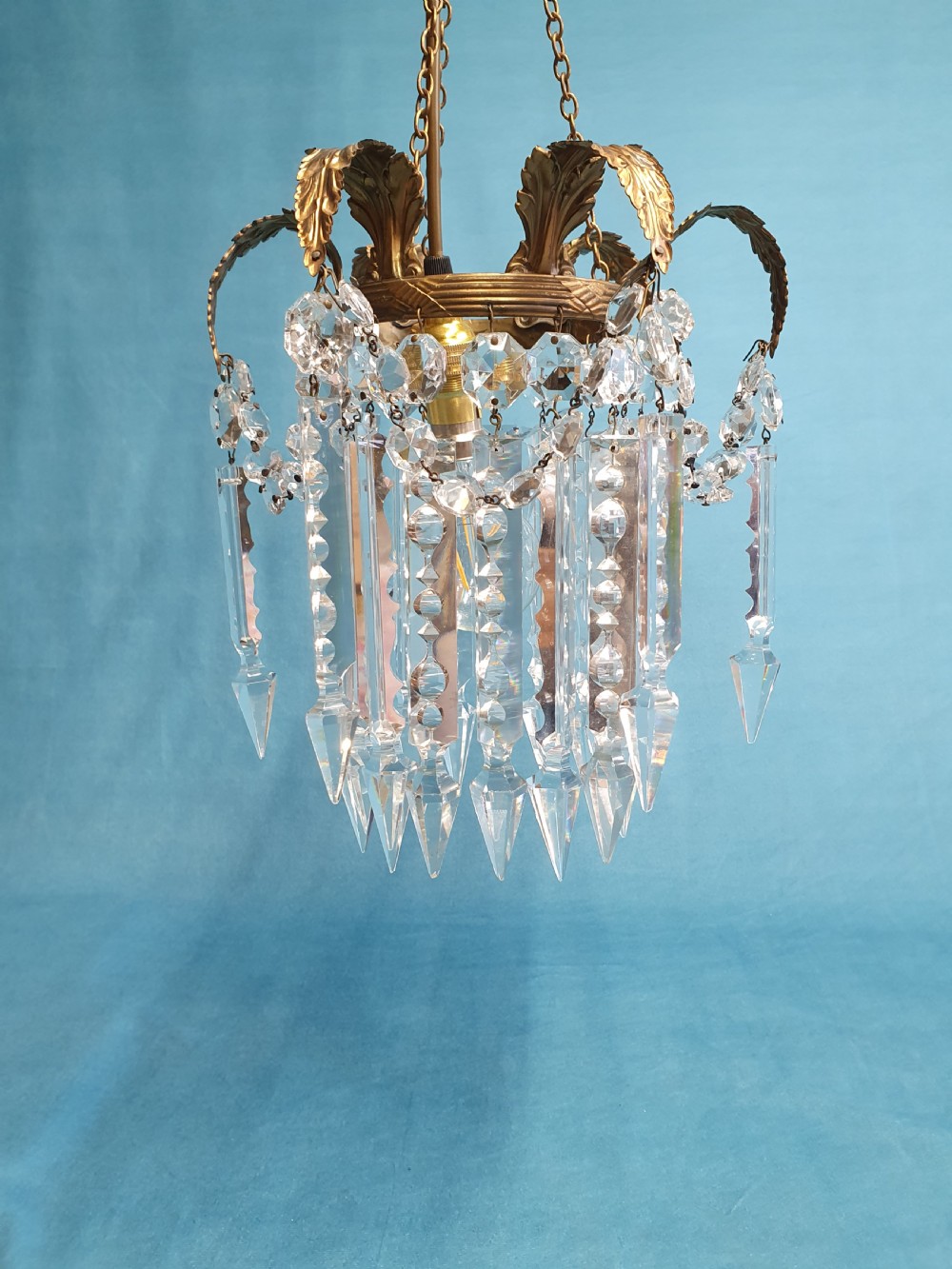 An early 20th-century small brass chandelier featuring acanthus leaf scroll arms suspending multiple tiers of clear faceted crystal prisms and droplets. View III