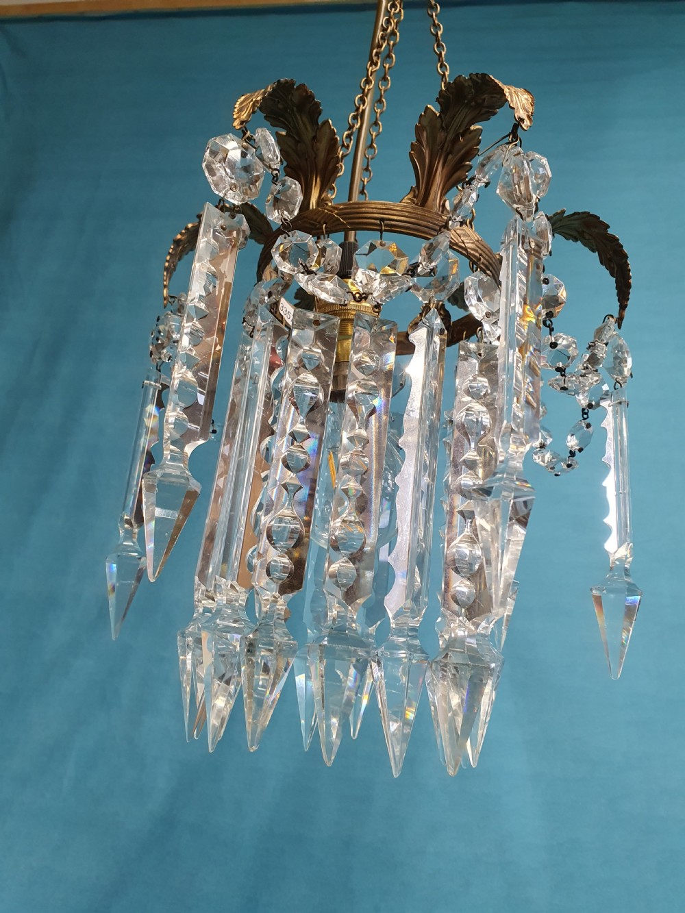 An early 20th-century small brass chandelier featuring acanthus leaf scroll arms suspending multiple tiers of clear faceted crystal prisms and droplets. View V