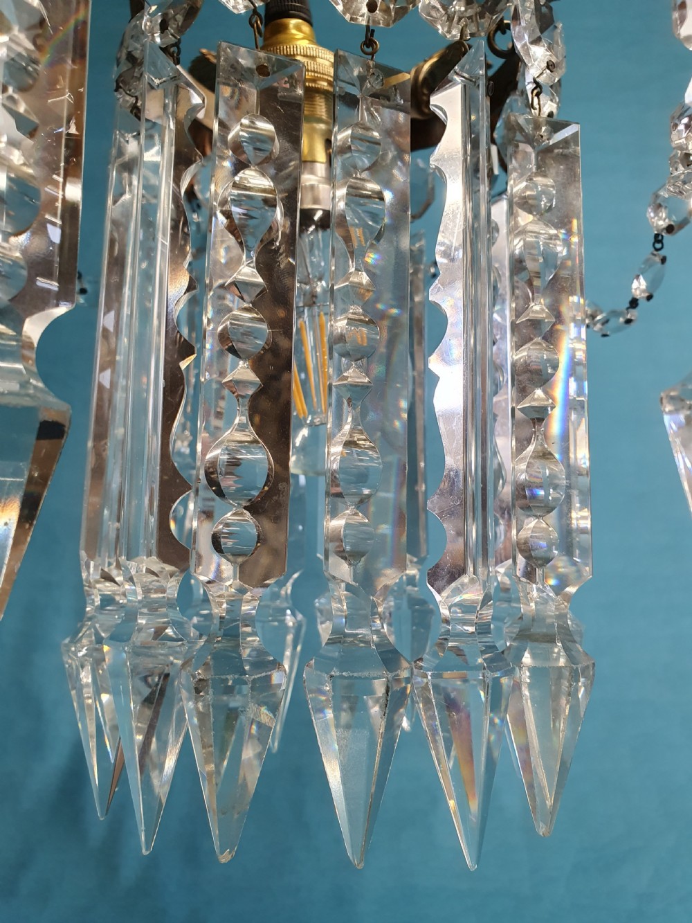 An early 20th-century small brass chandelier featuring acanthus leaf scroll arms suspending multiple tiers of clear faceted crystal prisms and droplets. View VI