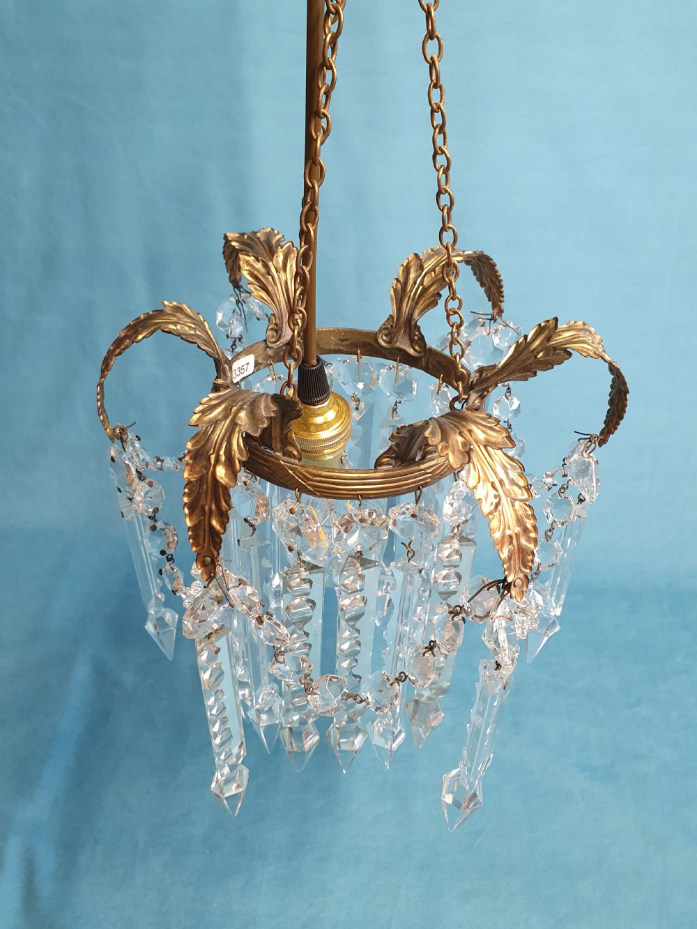 An early 20th-century small brass chandelier featuring acanthus leaf scroll arms suspending multiple tiers of clear faceted crystal prisms and droplets. View X
