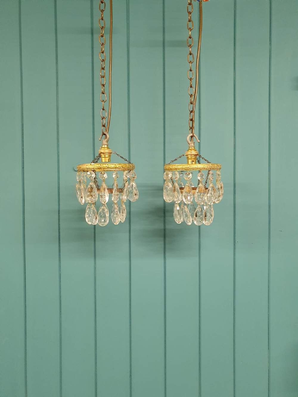 A pair of small early 20th-century brass ceiling pendant chandeliers featuring tiers of hanging faceted clear crystal droplets.
