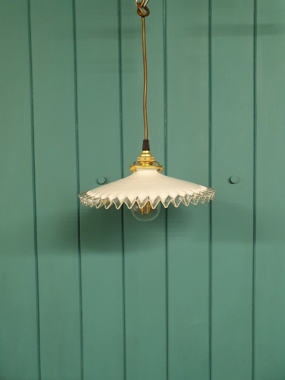 A white opaline glass pendant lampshade featuring a clear crimped frill edge suspended from a brass fixture.